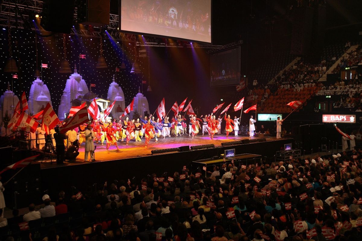 Devotees waving flags across a packed arena during a BAPS celebration assembly