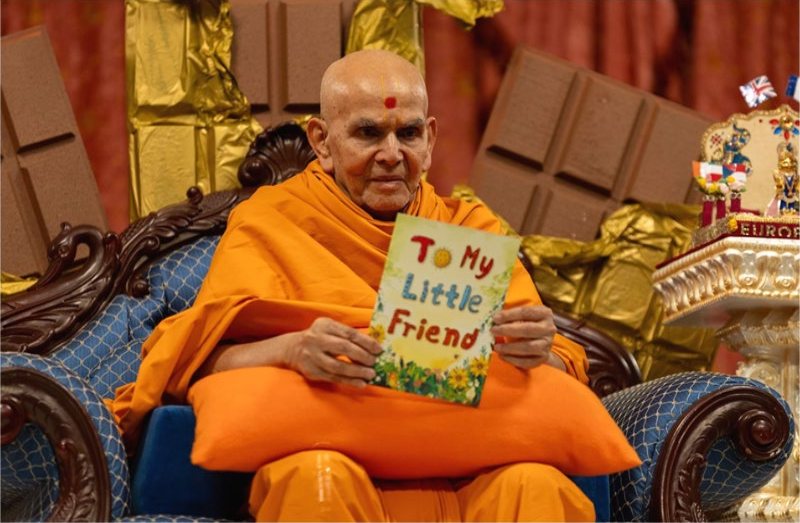 Mahant Swami Maharaj holding a children’s book during a Bal-Balika Din assembly