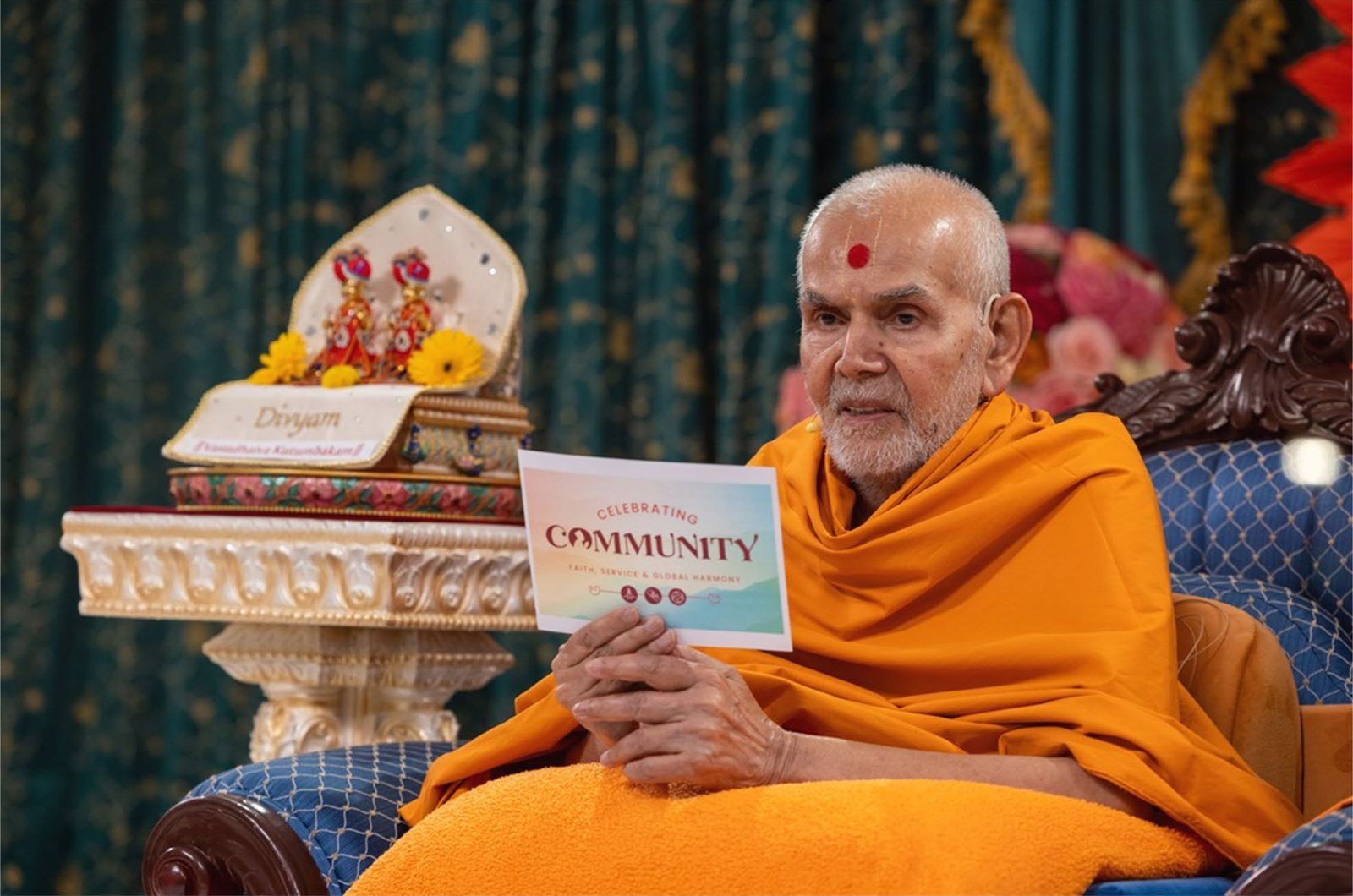 Mahant Swami Maharaj holding a Celebrating Community card during an assembly