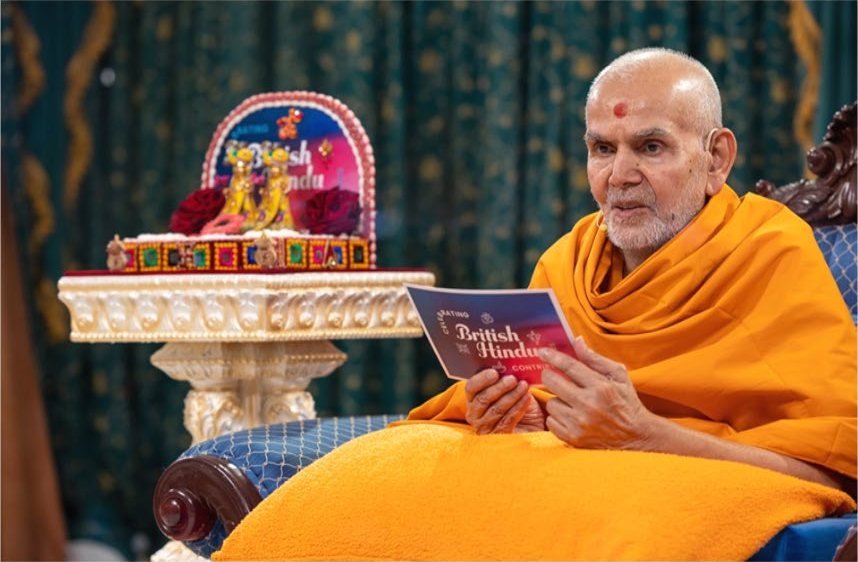 Mahant Swami Maharaj reading a booklet on British Hindu contributions