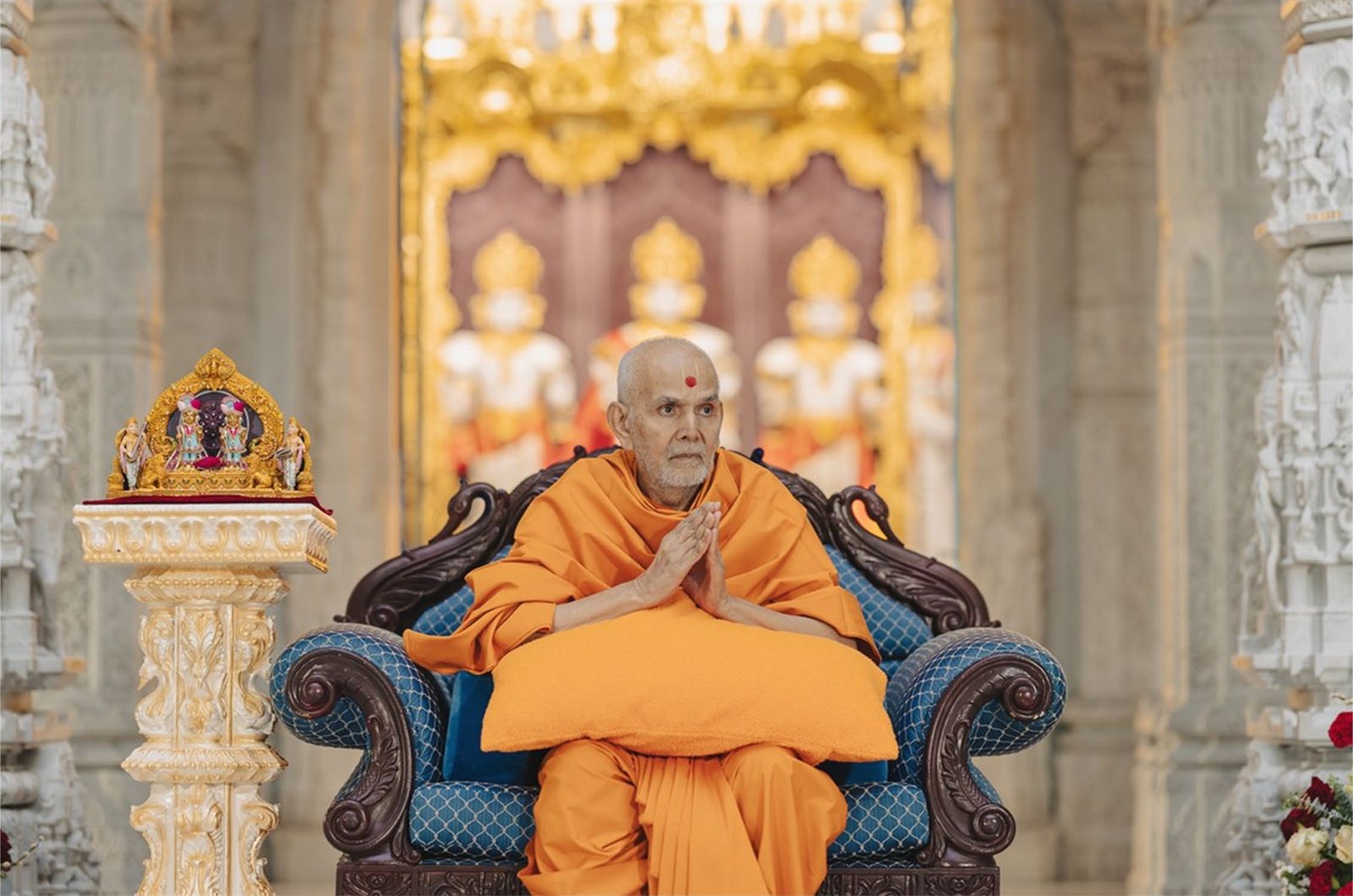 Mahant Swami Maharaj seated with folded hands before the murtis in the Mandir