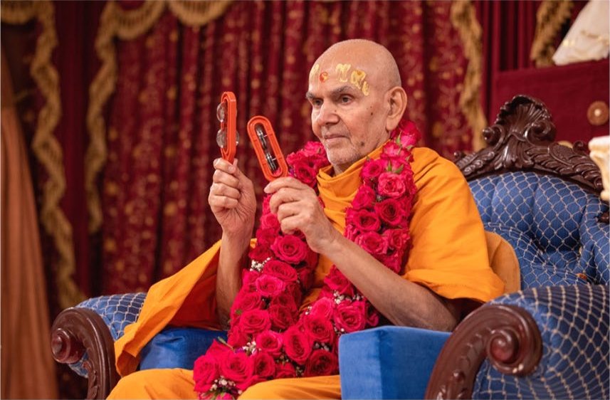 Mahant Swami Maharaj garlanded with roses, holding kartal during a kirtan