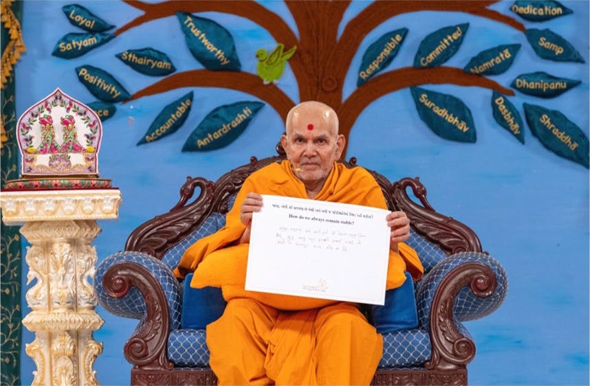 Mahant Swami Maharaj holding up a written answer before a backdrop of values