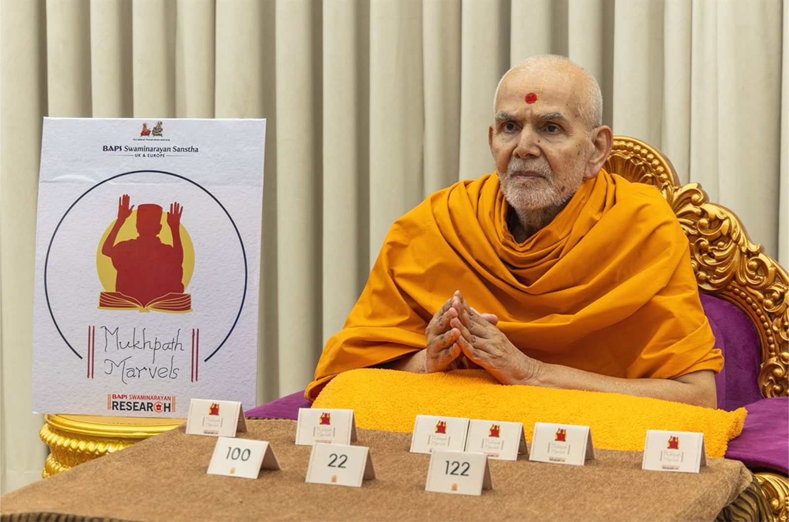 Mahant Swami Maharaj beside a Mukhpath Marvels poster with memorisation tallies before him