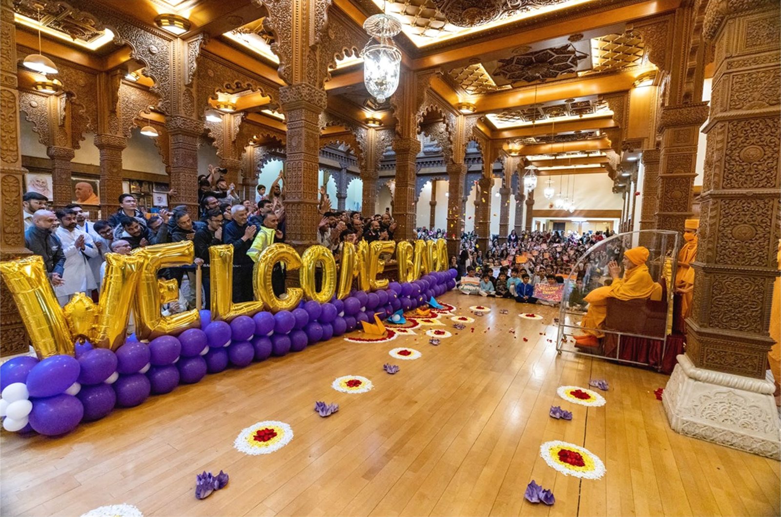Devotees welcoming Mahant Swami Maharaj into the haveli assembly hall with balloons and flower rangoli