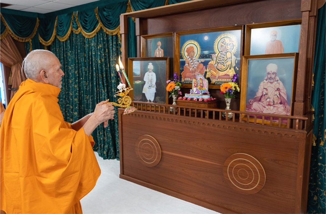 Mahant Swami Maharaj performing arti before framed images of the gurus