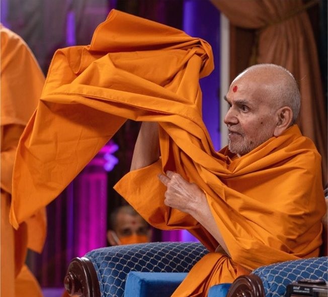 Mahant Swami Maharaj offering a length of saffron cloth during a ceremony
