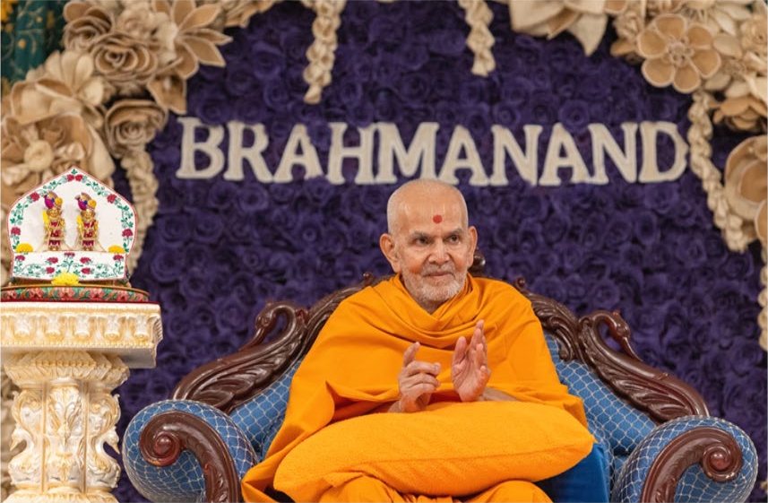 Mahant Swami Maharaj addressing a youth assembly before a floral backdrop